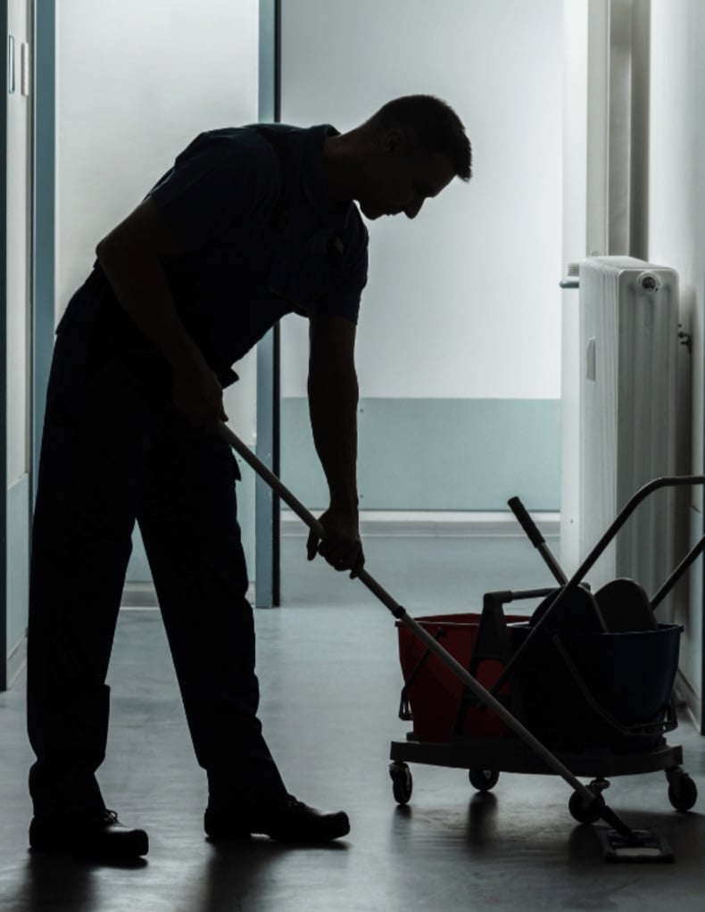 Custodian mopping a hallway floor beside a mop bucket cart
